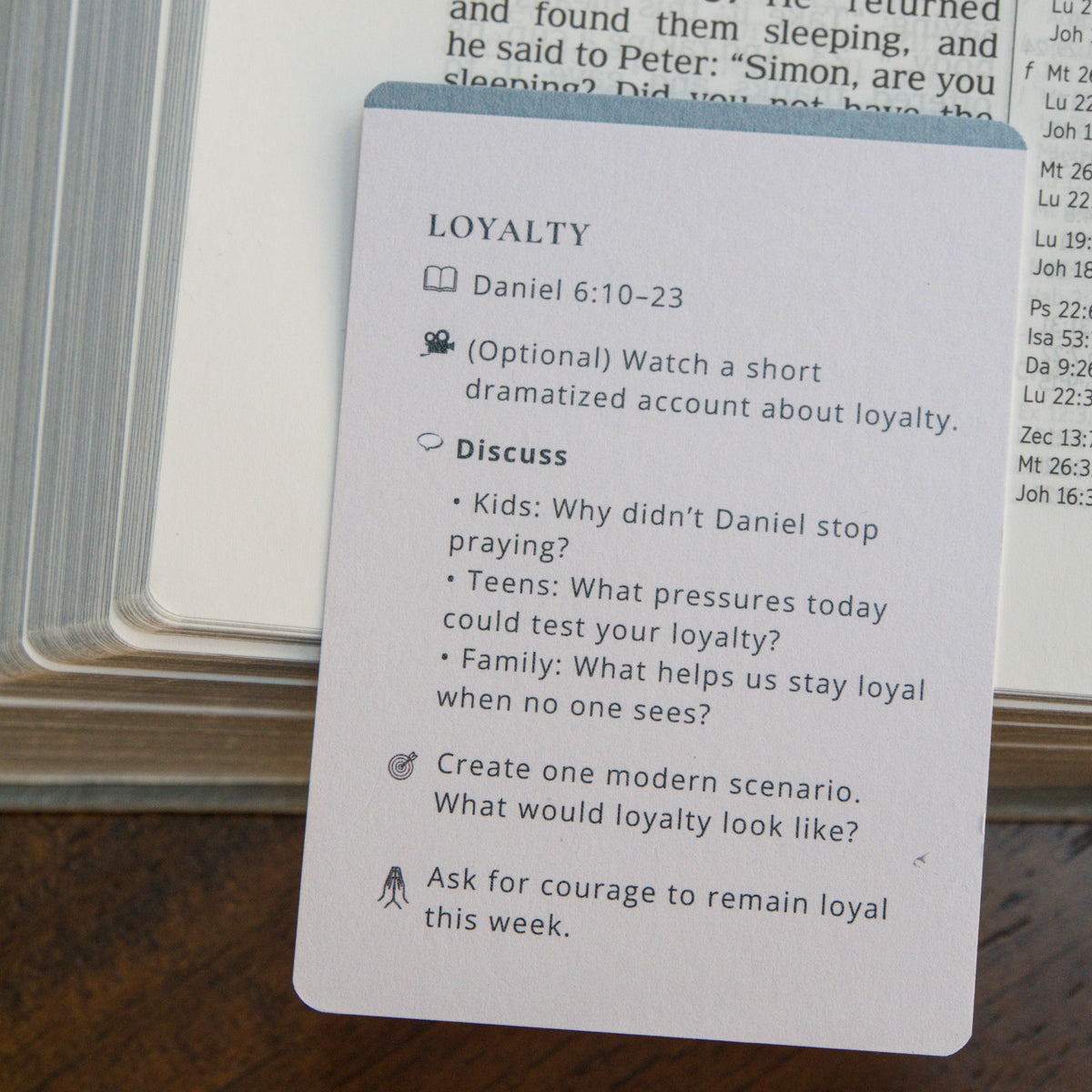 A white printed card with the heading 'LOYALTY' and bullet points for discussion and reflection, placed on top of an open Bible on a wooden surface.
